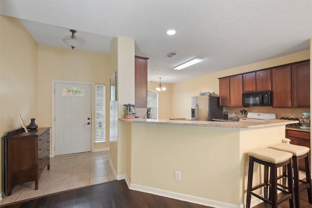 kitchen with range, kitchen peninsula, a kitchen breakfast bar, and stainless steel fridge with ice dispenser