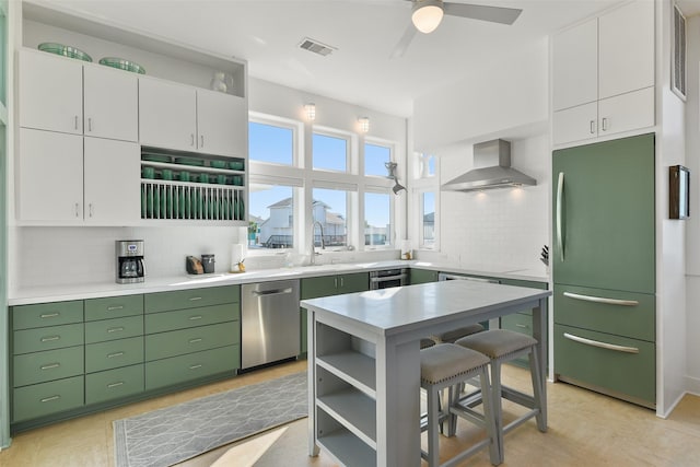 kitchen featuring visible vents, stainless steel dishwasher, refrigerator, green cabinets, and wall chimney range hood