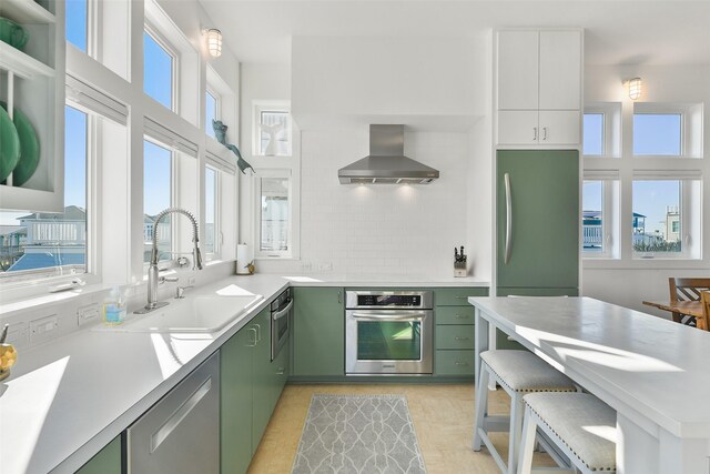 22823 Chiquita St, Galveston, TX 77554 - kitchen with green cabinetry, light countertops, a sink, appliances with stainless steel finishes, and wall chimney range hood