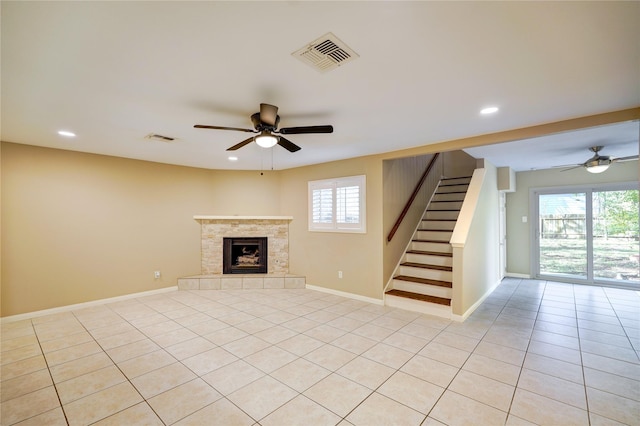 unfurnished living room with ceiling fan, a tiled fireplace, light tile patterned flooring, and a wealth of natural light