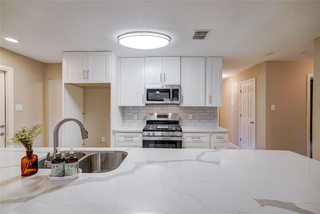 kitchen featuring stainless steel appliances, light stone countertops, white cabinets, backsplash, and sink