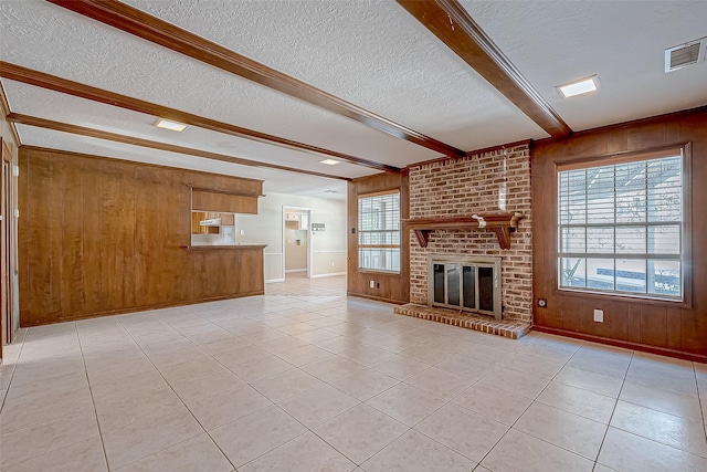 unfurnished living room with beam ceiling, wooden walls, and a brick fireplace