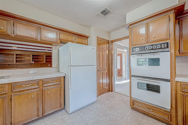 kitchen featuring tile counters, light tile patterned flooring, white appliances, and a textured ceiling