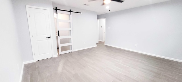 unfurnished bedroom with a barn door, ceiling fan, and light wood-type flooring