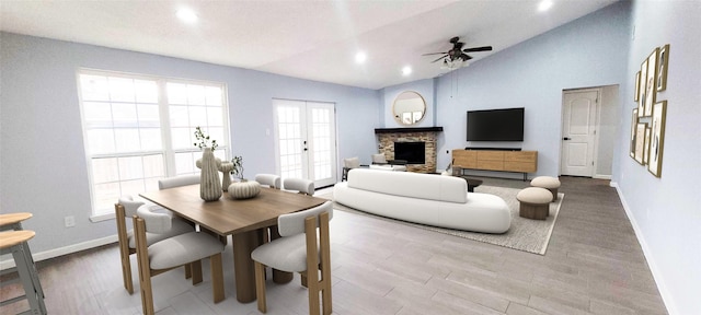 living room featuring lofted ceiling, ceiling fan, hardwood / wood-style floors, a stone fireplace, and french doors