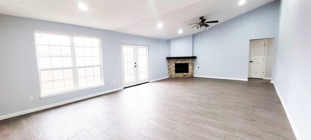 unfurnished living room featuring hardwood / wood-style flooring, ceiling fan, a stone fireplace, vaulted ceiling, and french doors