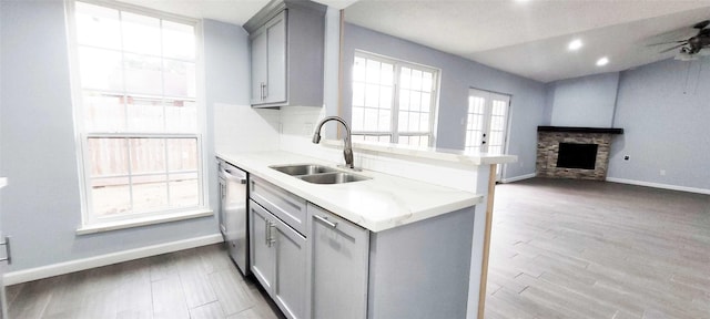 kitchen with a stone fireplace, sink, gray cabinetry, stainless steel dishwasher, and ceiling fan