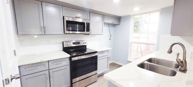 kitchen featuring sink, decorative backsplash, light stone countertops, and appliances with stainless steel finishes