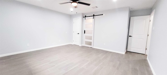 unfurnished bedroom with light hardwood / wood-style flooring, a barn door, and ceiling fan