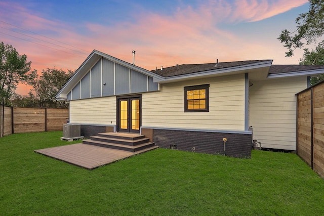 back house at dusk featuring french doors, a yard, central AC, and a deck