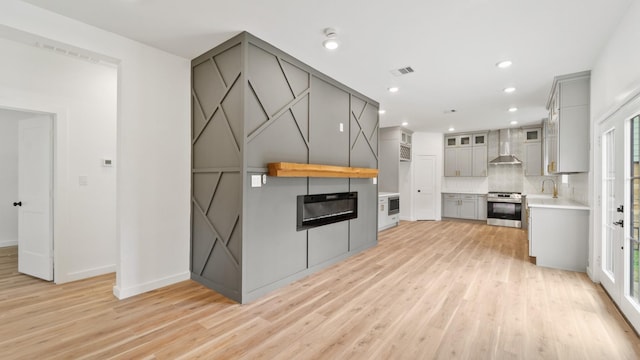 kitchen featuring gray cabinetry, stainless steel range, wall chimney range hood, backsplash, and light hardwood / wood-style floors