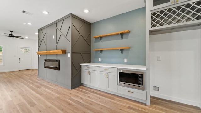 kitchen with white cabinets, light hardwood / wood-style flooring, ceiling fan, and built in microwave