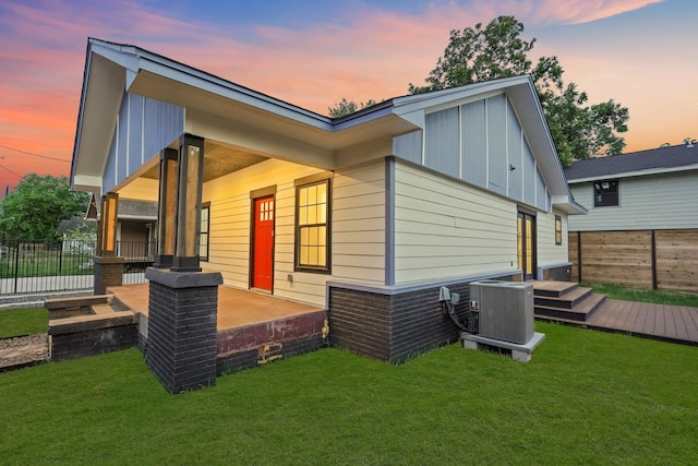 back house at dusk featuring a patio, a yard, and central AC