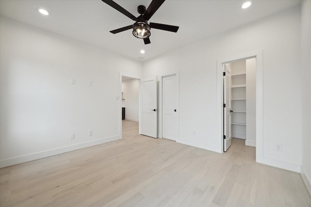 unfurnished bedroom featuring ceiling fan, a closet, a walk in closet, and light wood-type flooring