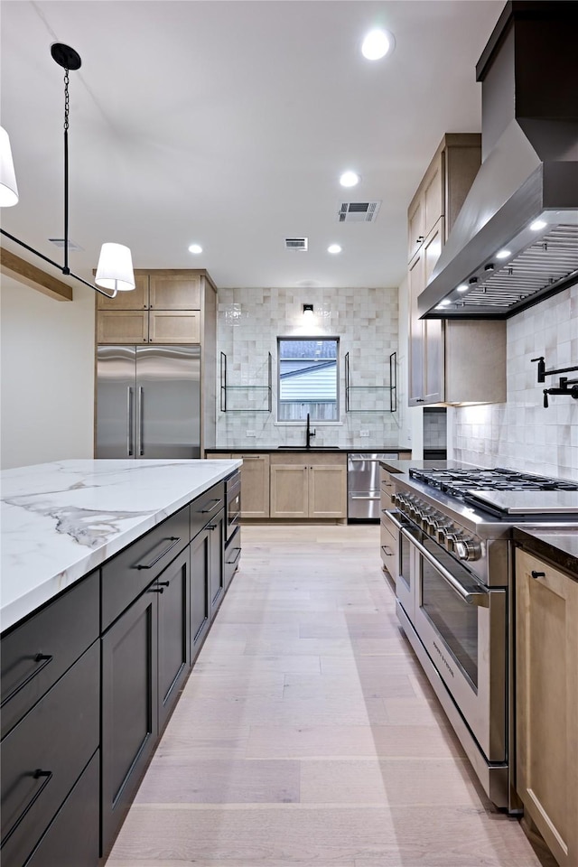 kitchen featuring backsplash, pendant lighting, built in appliances, island range hood, and light stone counters