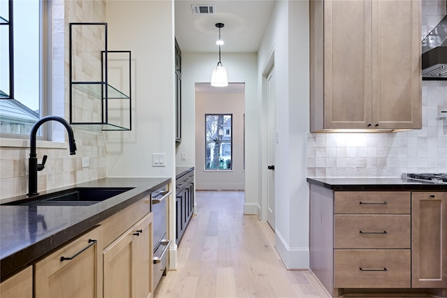 kitchen with sink, backsplash, light wood-type flooring, and hanging light fixtures