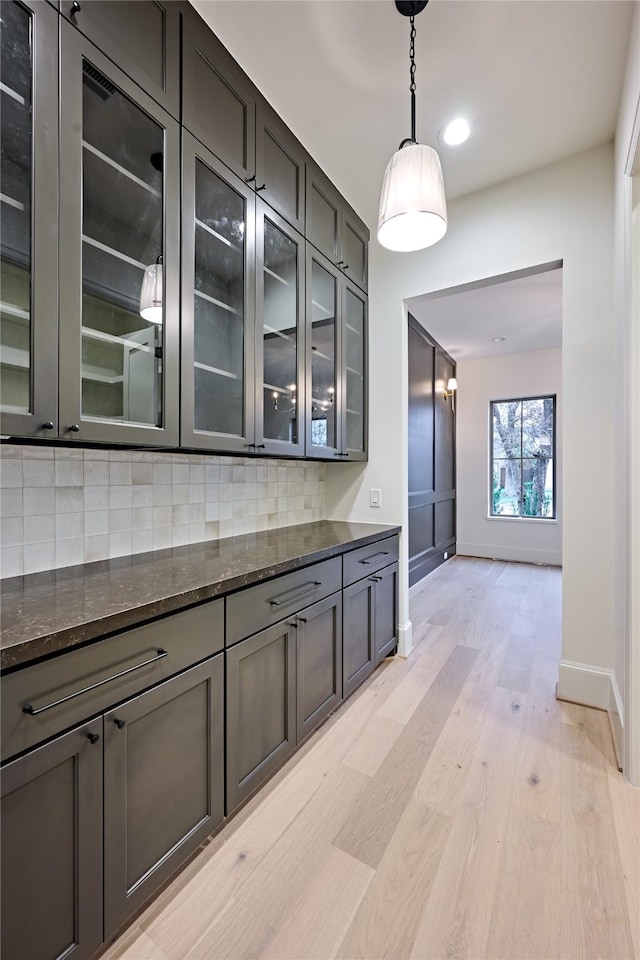 interior space with decorative backsplash, dark stone countertops, light hardwood / wood-style floors, and decorative light fixtures