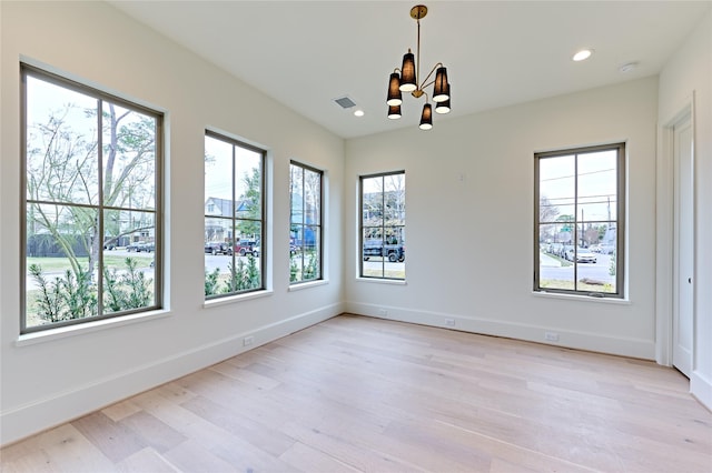 spare room featuring an inviting chandelier and light hardwood / wood-style floors