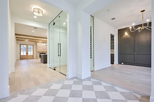 hall with a chandelier, light hardwood / wood-style flooring, french doors, and beamed ceiling