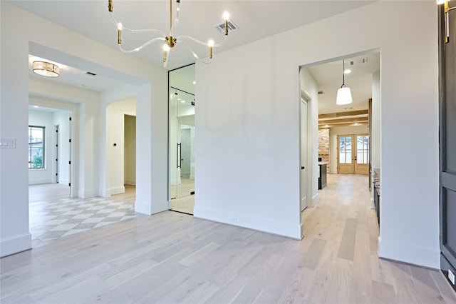 spare room with light wood-type flooring, french doors, a notable chandelier, and a wealth of natural light