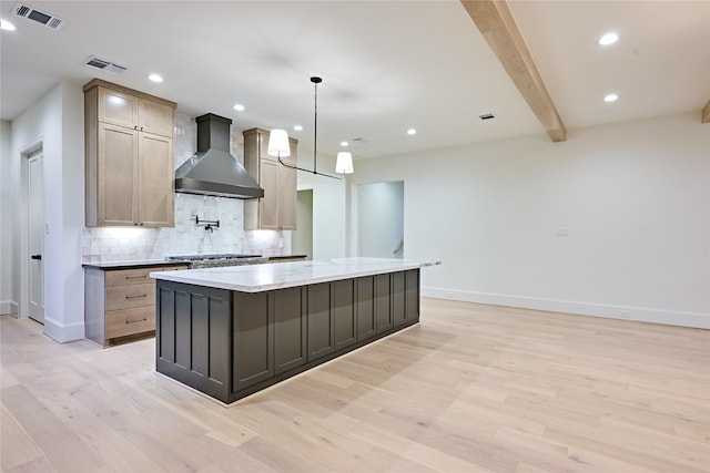 kitchen featuring beamed ceiling, wall chimney range hood, light hardwood / wood-style floors, and a kitchen island