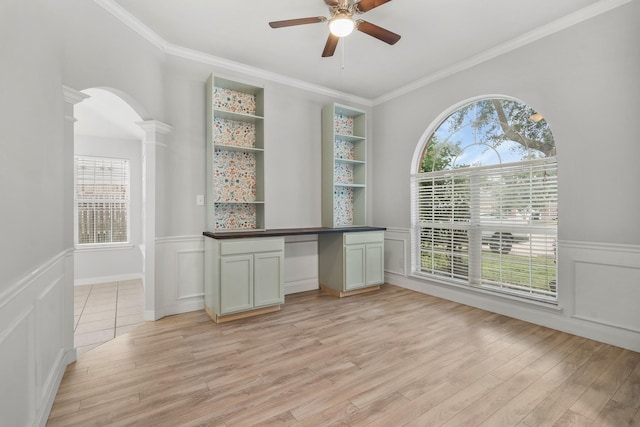 unfurnished dining area with built in shelves, ceiling fan, light wood-type flooring, and decorative columns