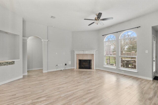 unfurnished living room featuring ceiling fan, light hardwood / wood-style floors, a fireplace, and decorative columns