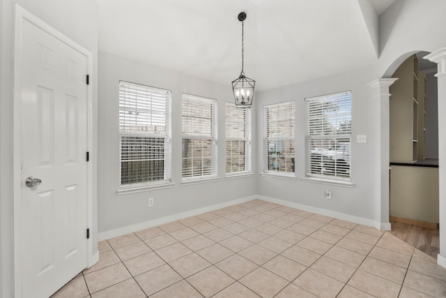 unfurnished dining area featuring light tile patterned floors, decorative columns, and an inviting chandelier