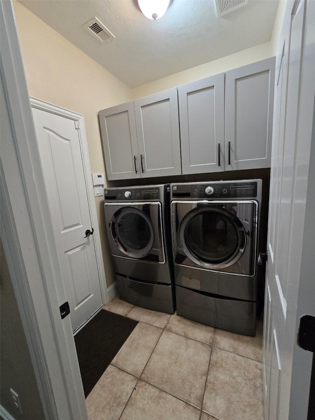 laundry room featuring washer and dryer, cabinets, and light tile patterned floors