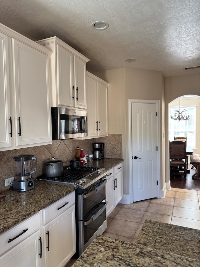 kitchen with light tile patterned floors, white cabinetry, dark stone countertops, and appliances with stainless steel finishes