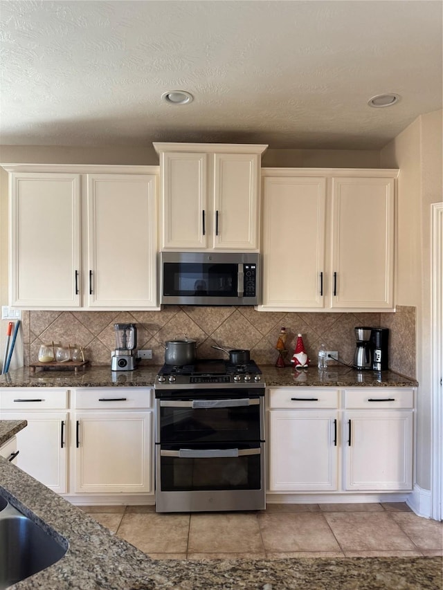 kitchen featuring sink, decorative backsplash, dark stone countertops, white cabinetry, and stainless steel appliances