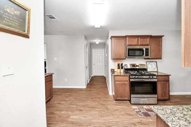 kitchen with stone counters, stainless steel appliances, and light hardwood / wood-style floors