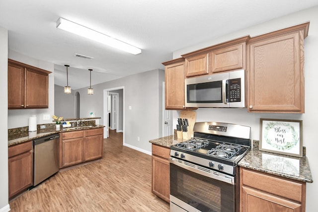 kitchen with dark stone counters, sink, light wood-type flooring, appliances with stainless steel finishes, and decorative light fixtures