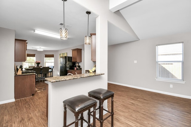 kitchen featuring pendant lighting, dark wood-type flooring, black refrigerator, vaulted ceiling, and kitchen peninsula