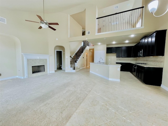 kitchen featuring ceiling fan, a towering ceiling, an island with sink, decorative backsplash, and a fireplace