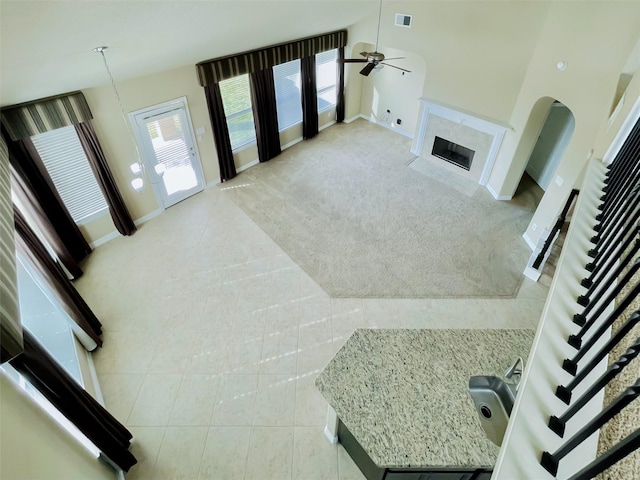 living room with ceiling fan, a fireplace, light colored carpet, and a high ceiling