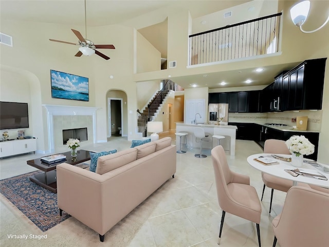 tiled living room with a tile fireplace, ceiling fan, sink, and a high ceiling