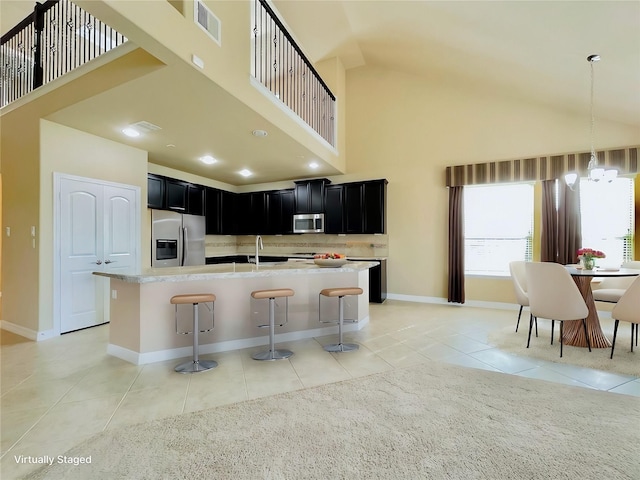 kitchen with sink, a kitchen island with sink, a breakfast bar, light tile patterned flooring, and appliances with stainless steel finishes