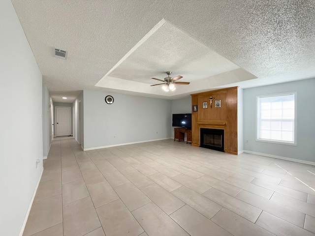 unfurnished living room with a textured ceiling, ceiling fan, a fireplace, and a tray ceiling