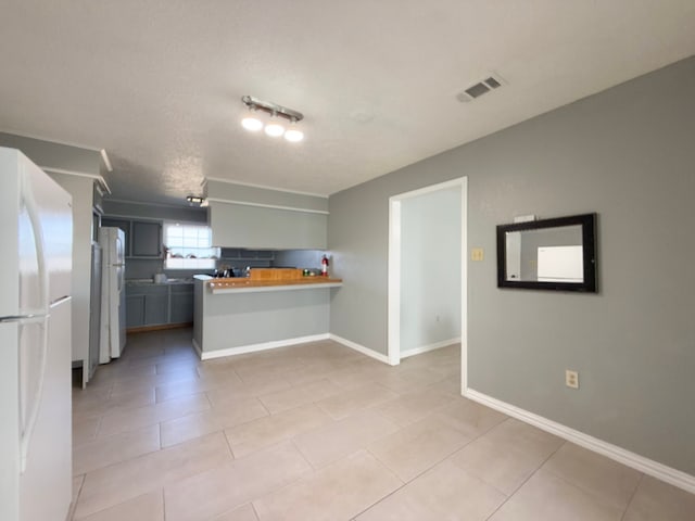 kitchen with a kitchen bar, kitchen peninsula, white refrigerator, and wood counters