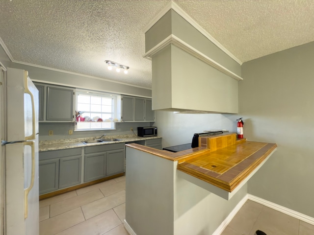 kitchen with white refrigerator, sink, light tile patterned floors, a textured ceiling, and kitchen peninsula