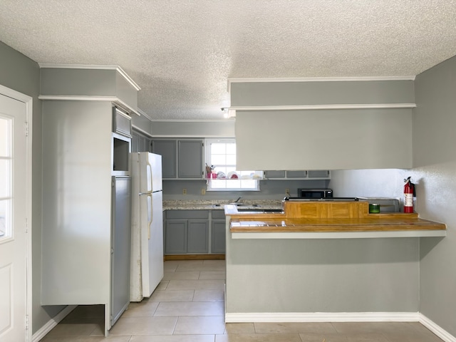 kitchen with gray cabinetry, wooden counters, light tile patterned floors, white fridge, and kitchen peninsula