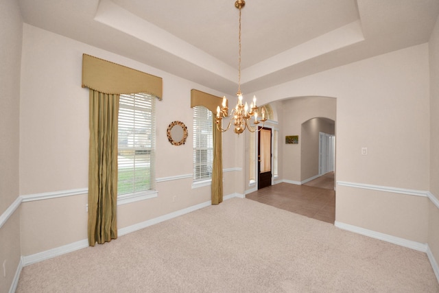 spare room with an inviting chandelier, a raised ceiling, and carpet floors