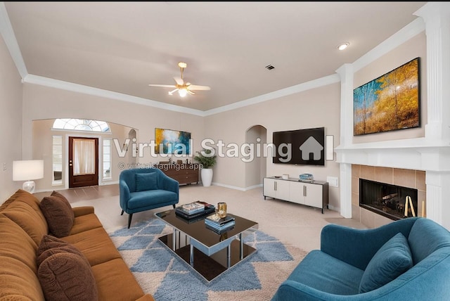 carpeted living room with arched walkways, a tile fireplace, visible vents, baseboards, and crown molding