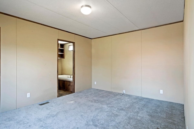 unfurnished bedroom featuring dark carpet, ornamental molding, a textured ceiling, and ensuite bath