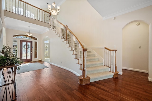 entryway with a towering ceiling, dark hardwood / wood-style floors, ornamental molding, and a notable chandelier