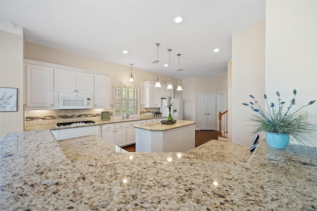 kitchen with white appliances, white cabinets, a center island, hanging light fixtures, and light stone counters