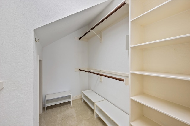 walk in closet with light carpet and vaulted ceiling