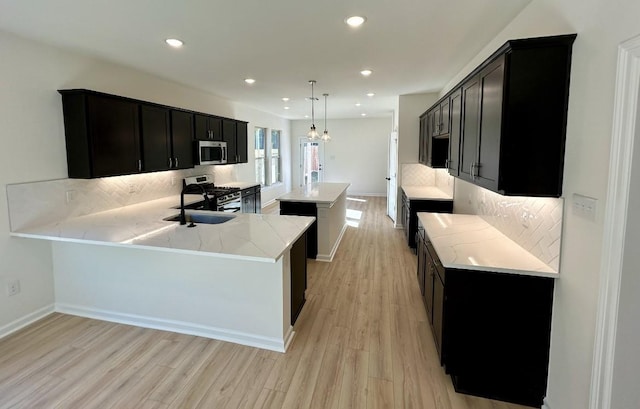 kitchen with appliances with stainless steel finishes, decorative light fixtures, kitchen peninsula, and backsplash