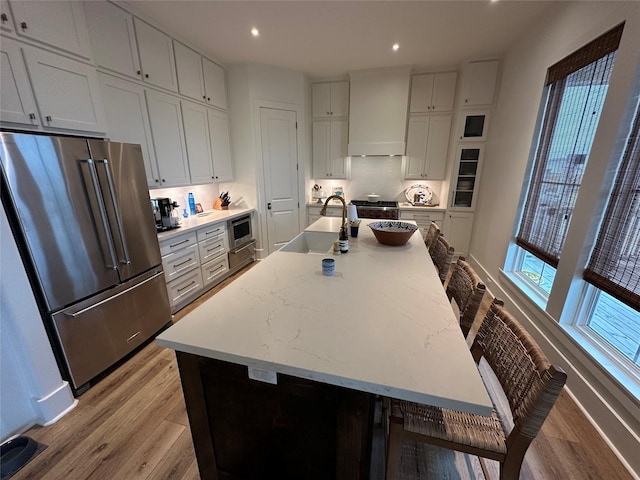 kitchen featuring high end fridge, wall chimney range hood, sink, and an island with sink